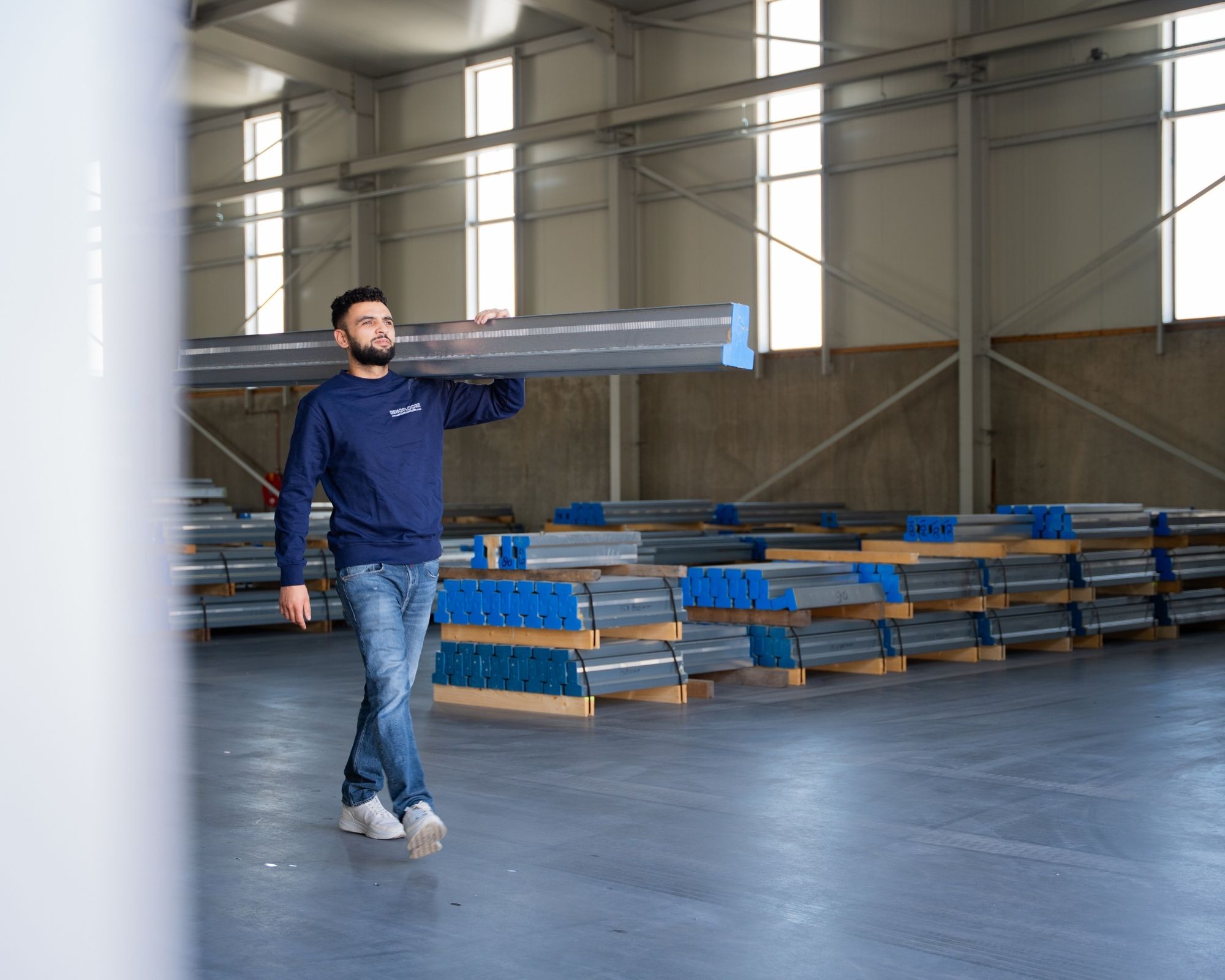 Medewerker van Renofloorz draagt een stalen ligger door het magazijn